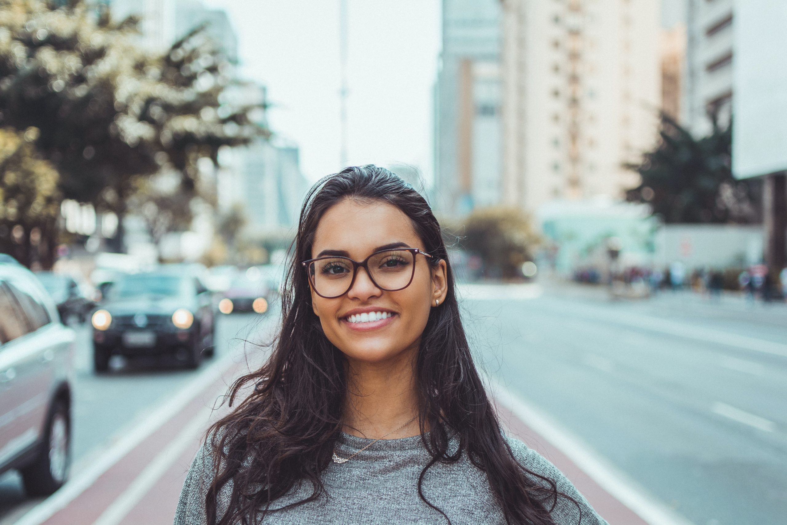 a woman standing on a street, smiling and is wearing glasses