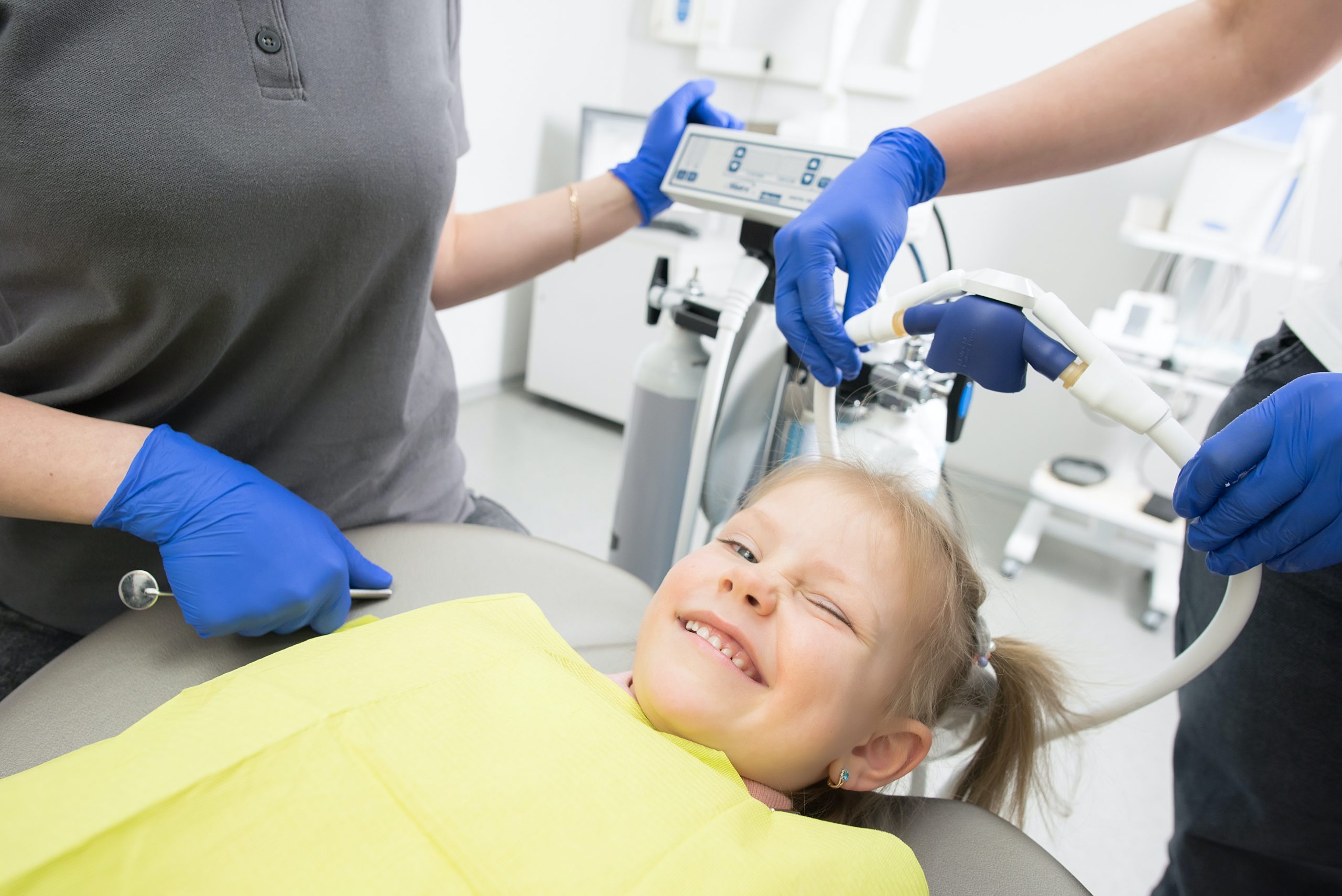 a female child smiles and winks at the camera as she lays in the dentist chair.