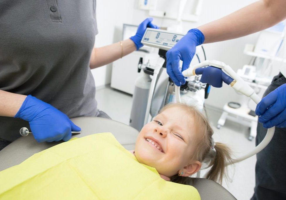 a female child smiles and winks at the camera as she lays in the dentist chair.